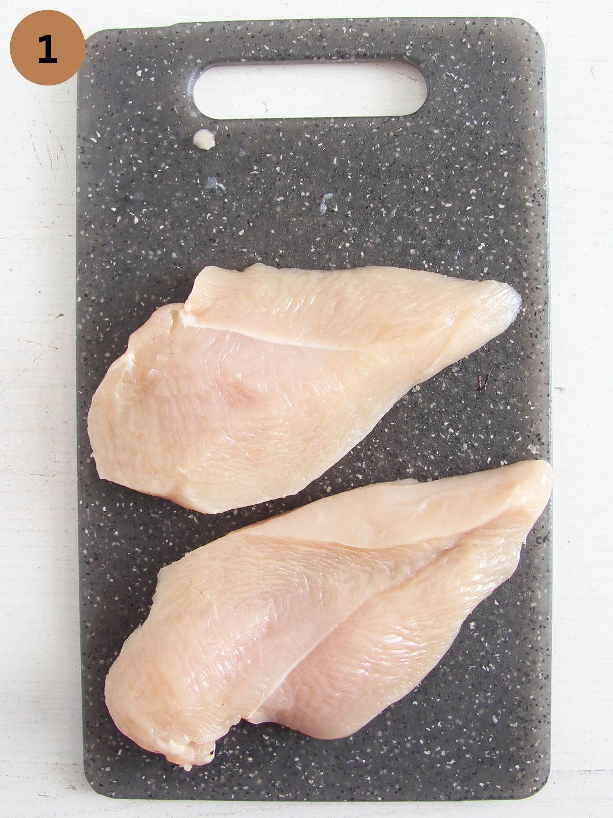 two raw chicken fillets on a gray cutting board.