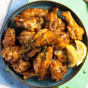 honey garlic chicken wings in a bowl with lemon wedges.