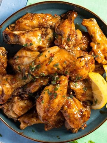 honey garlic chicken wings in a bowl with lemon wedges.