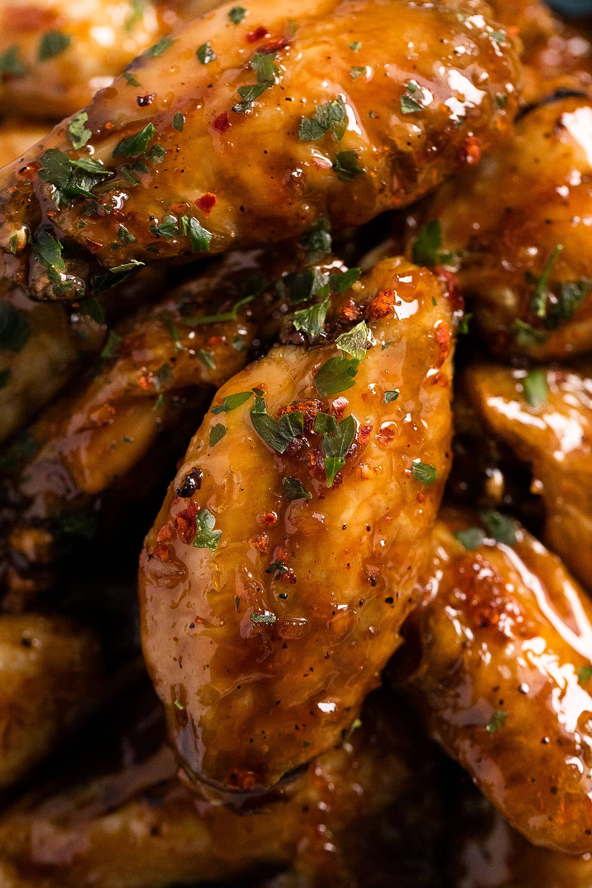 close up of glazed and shiny chicken wings sprinkled with parsley.