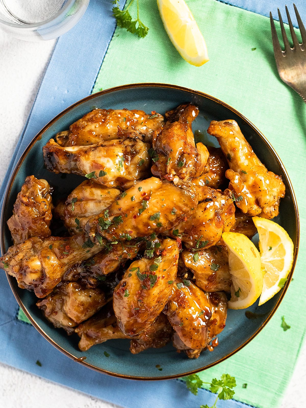 bowl of chicken wings glazed with sauce on a blue green cloth.