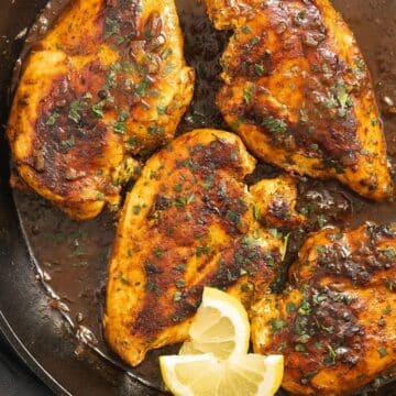 four small sauteed chicken breast and two lemon slices in a pan.