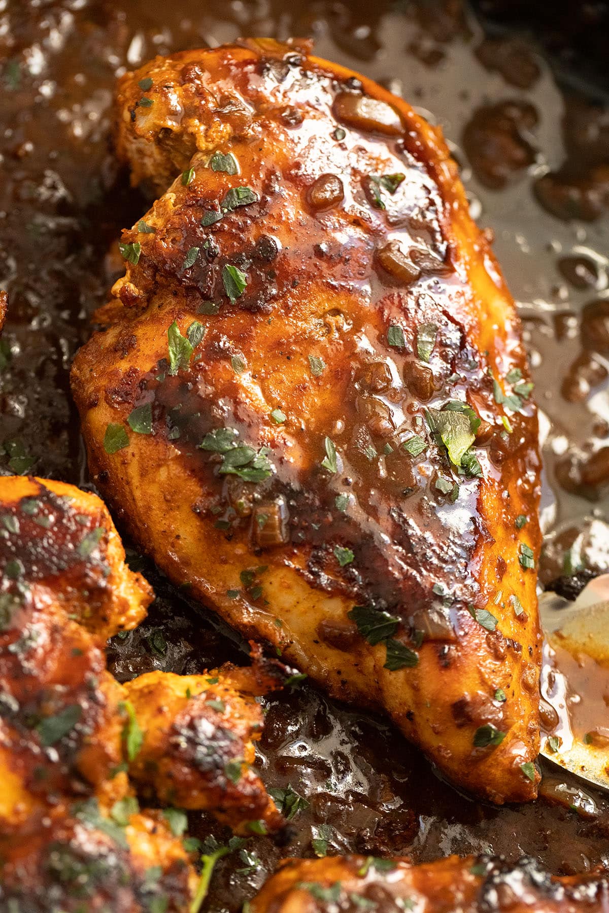 one golden brown chicken breast seared in the pan and covered with pan sauce.