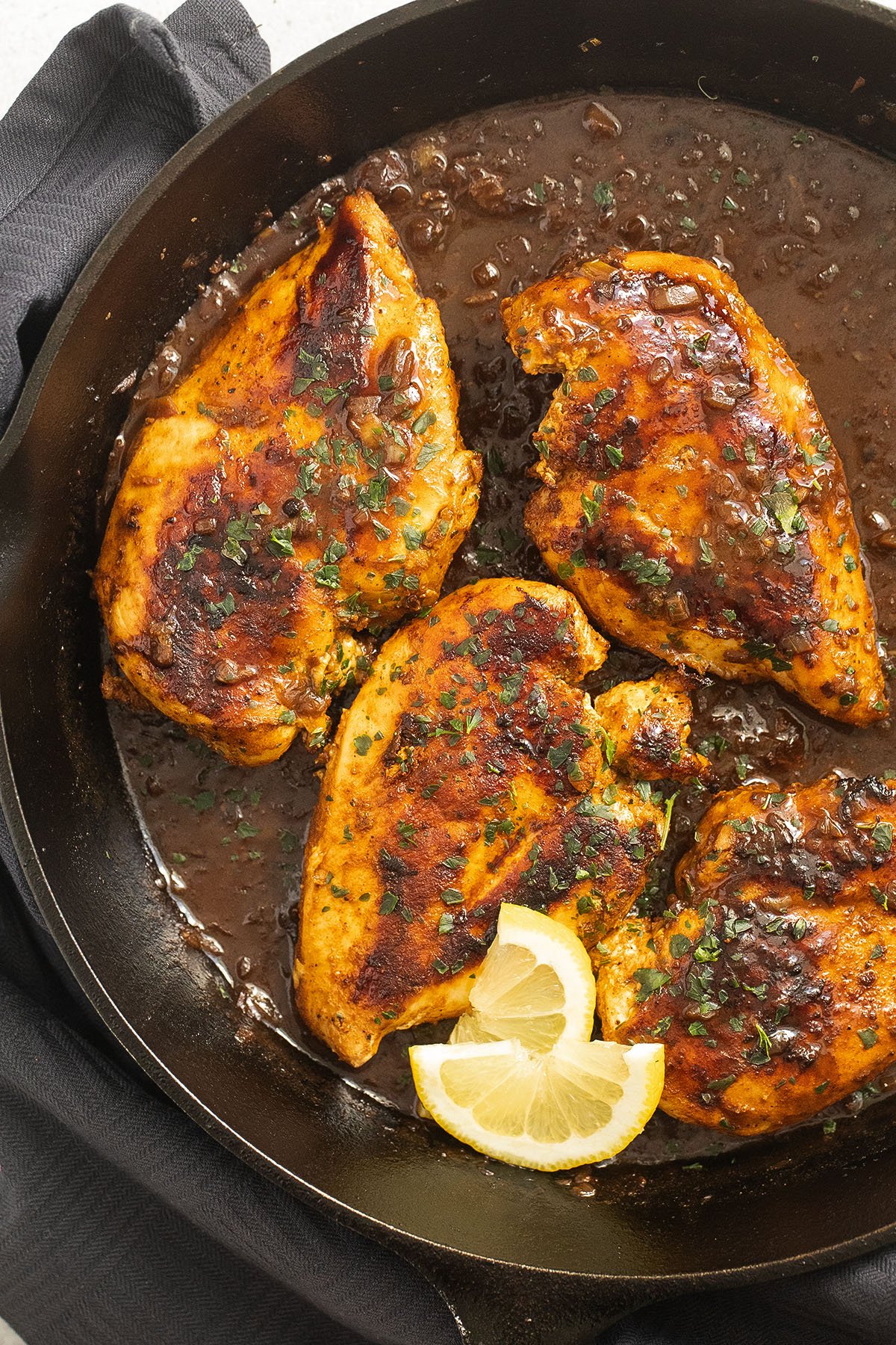 four golden brown chicken breasts sauteed in a cast iron skillet.