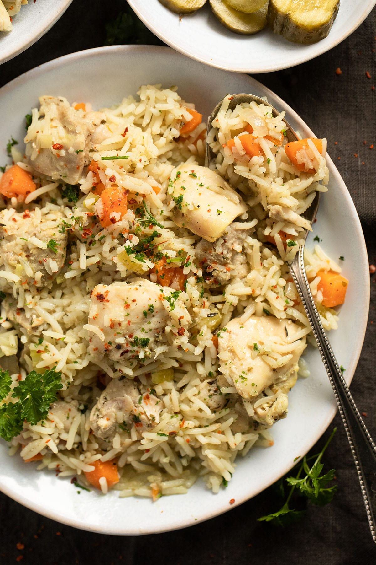 plate full of chicken and rice with carrots and a spoon in it.