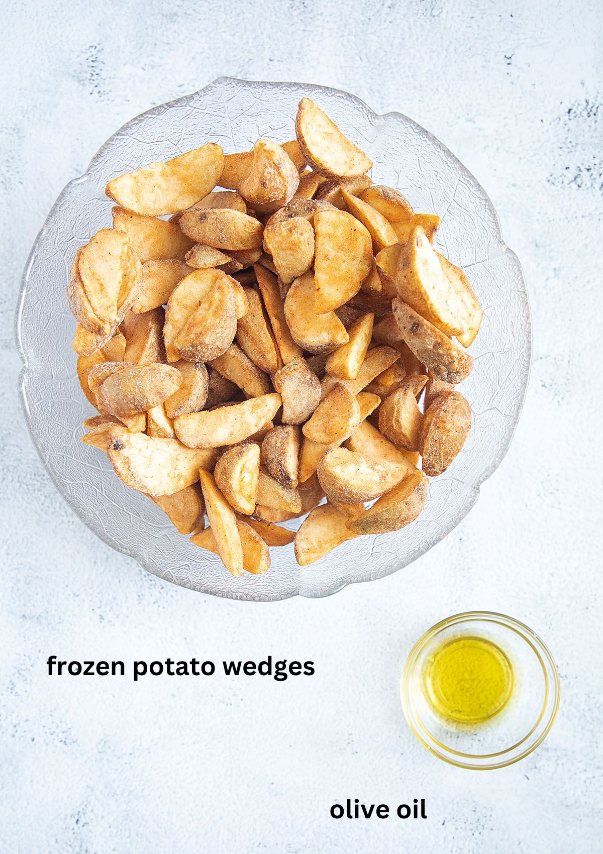 a bowl of uncooked frozen potato wedges and a small bowl with olive oil.