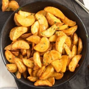 a bowl of air fryer frozen potato wedges on a black cloth.