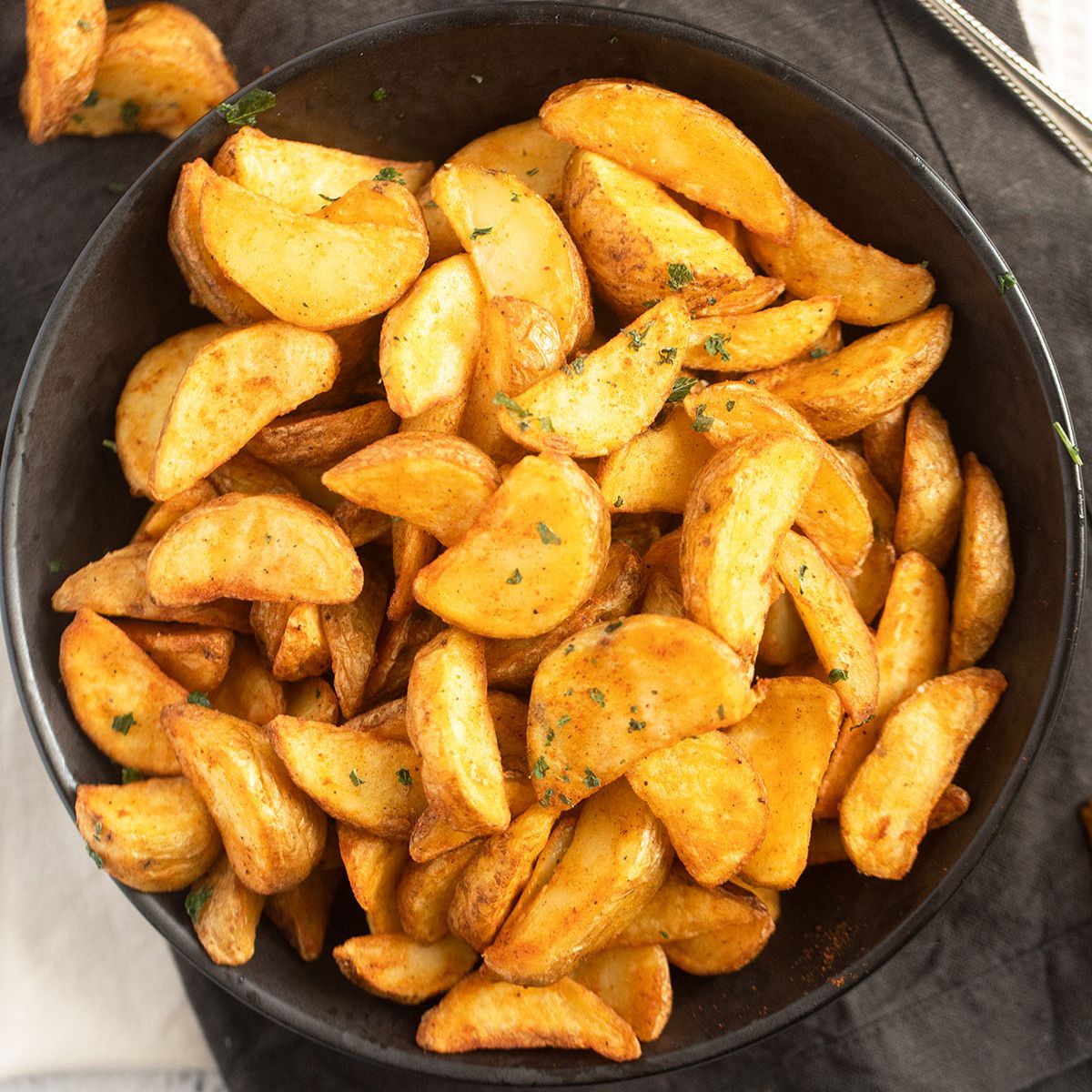 a bowl of air fryer frozen potato wedges on a black cloth.
