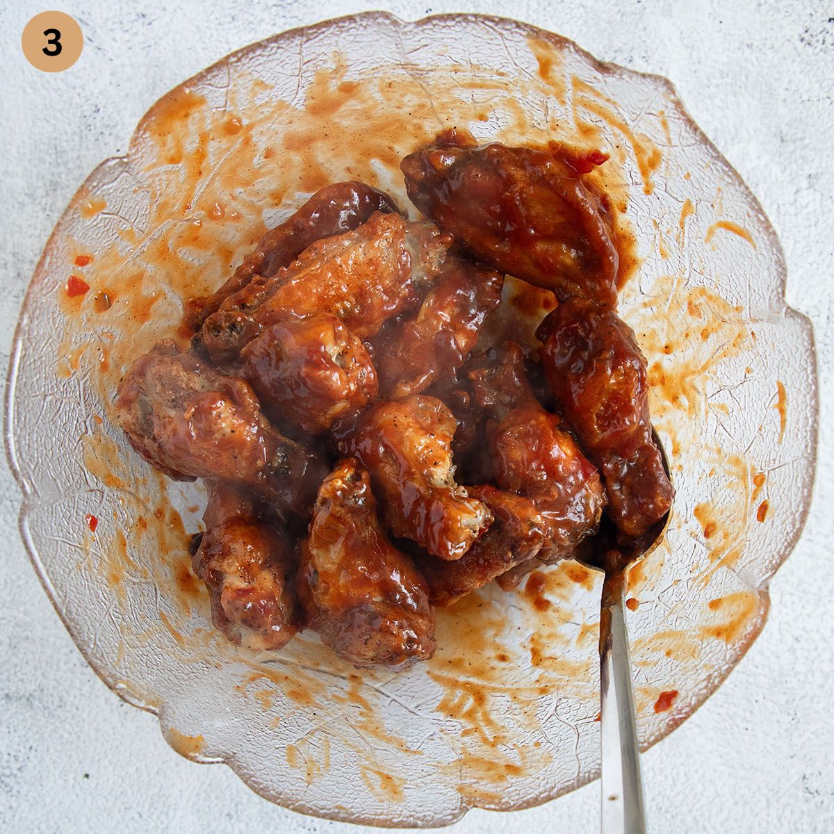 tossing wings with bbq sauce in a bowl with a spoon.