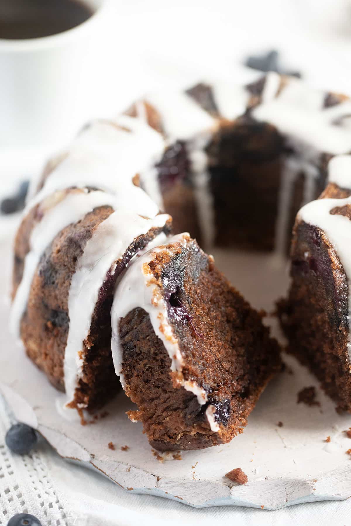 sliced bundt cake with sour cream and blueberries on a white round cutting board.