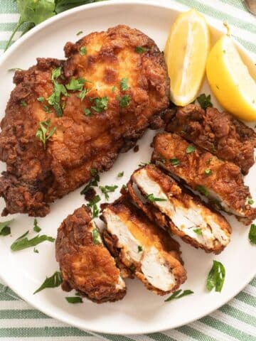two pieces of sliced fried chicken breast and lemon wedges on a plate.