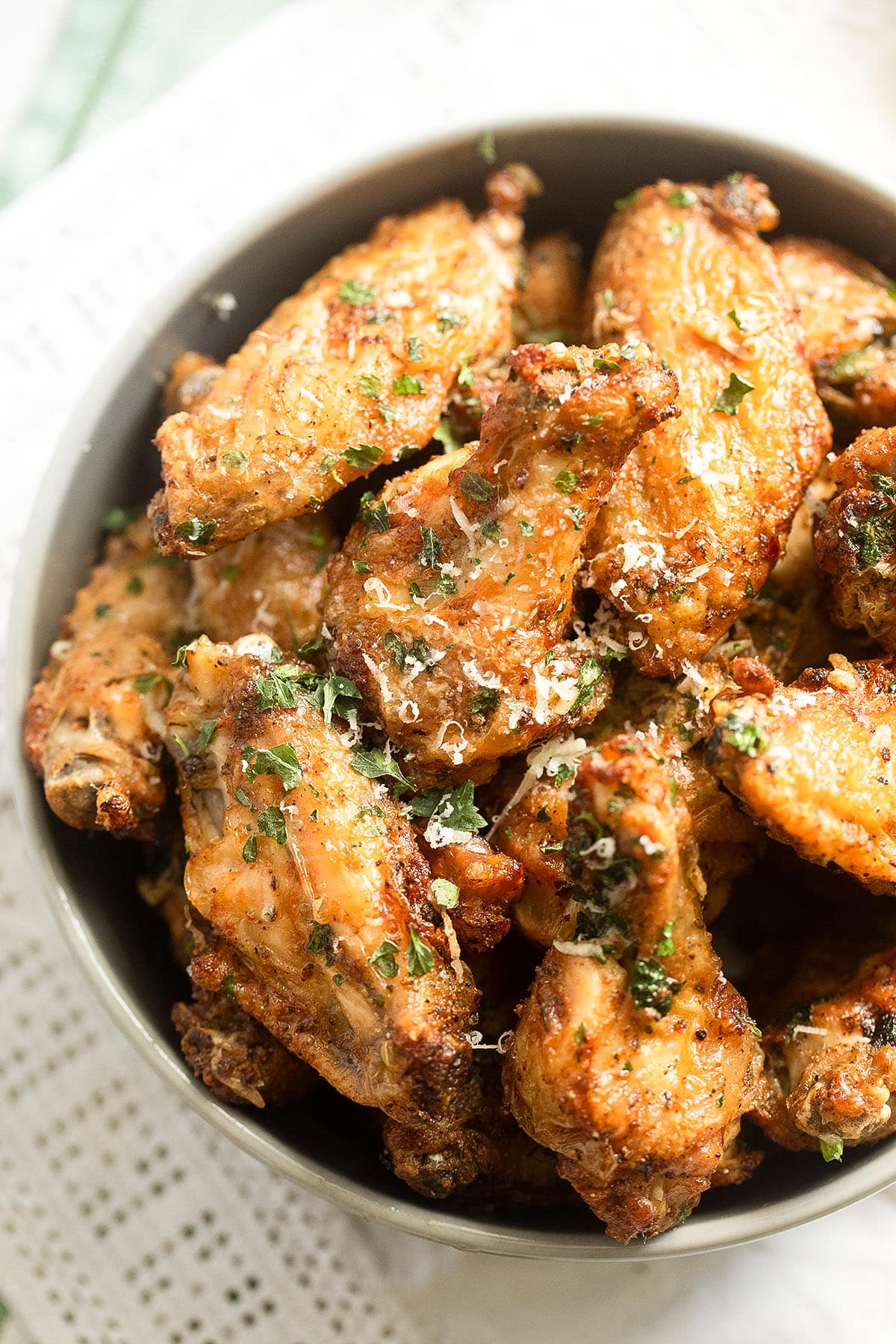 garlic parm wings in a bowl, sprinkled with parsley and cheese.