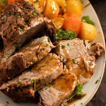 sliced instant pot pork roast drizzled with gravy and sprinkled with parsley.