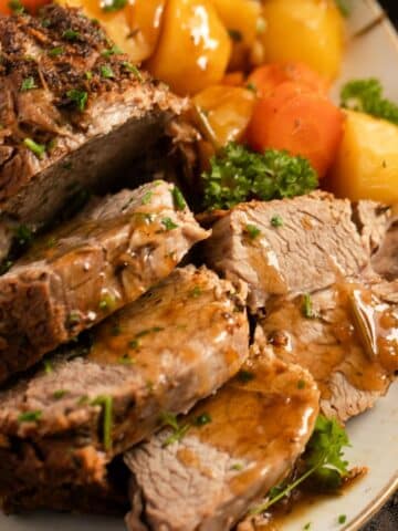 sliced instant pot pork roast drizzled with gravy and sprinkled with parsley.