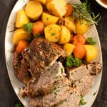 overhead view of a large oval platter with sliced pork roast, potatoes and carrots.