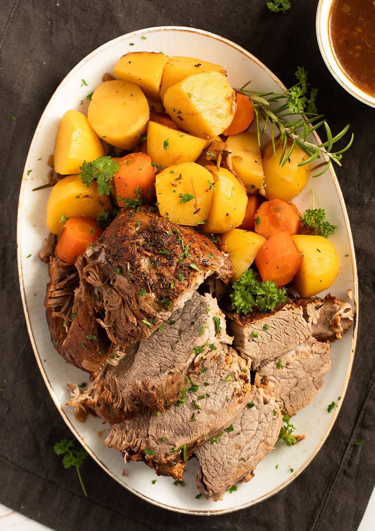 overhead view of a large oval platter with sliced pork roast, potatoes and carrots.