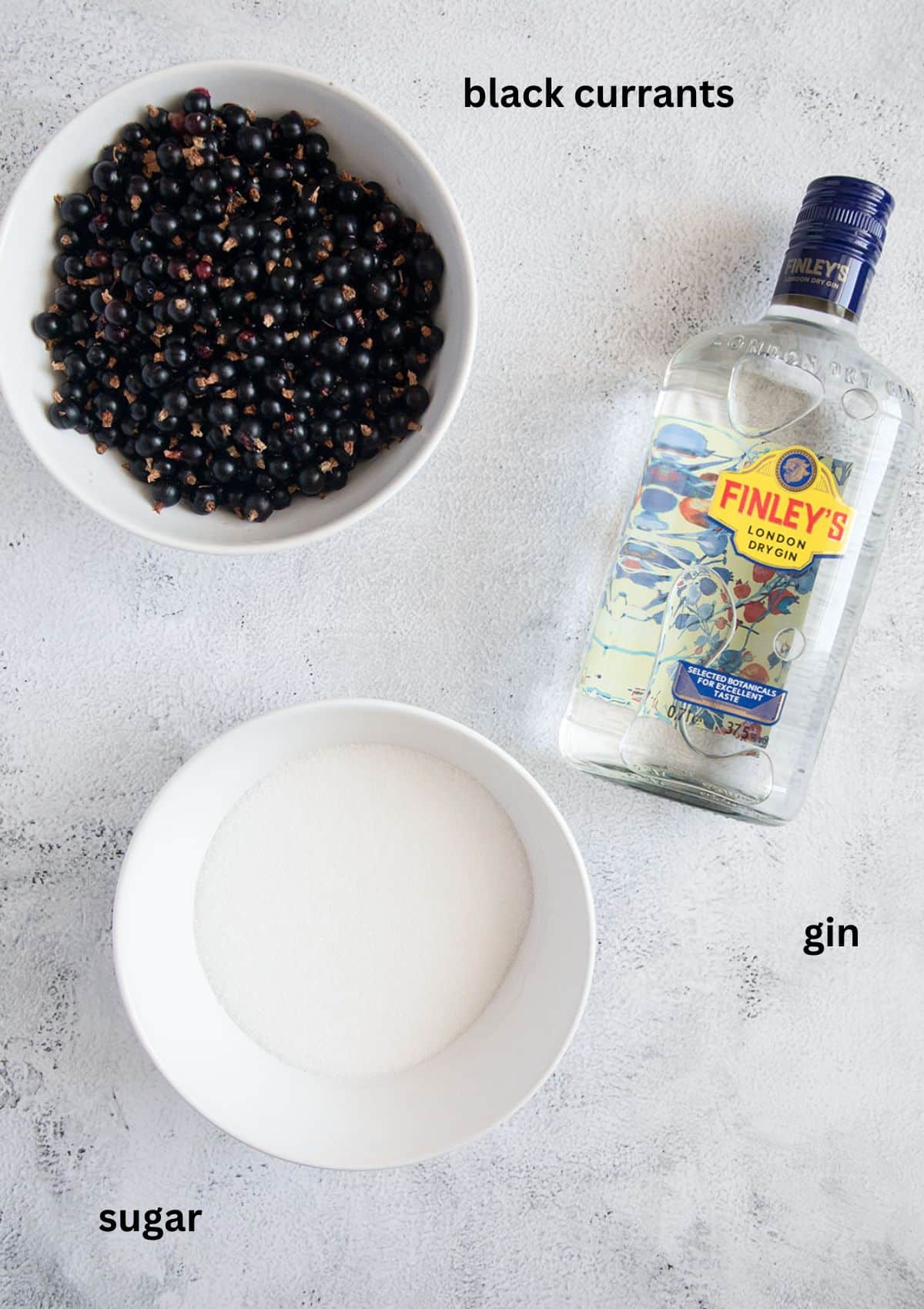 bowls with black currants and sugar and a bottle of gin.