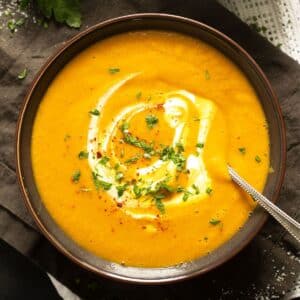 spicy carrot and lentil soup served with a little yogurt in a brown bowl.