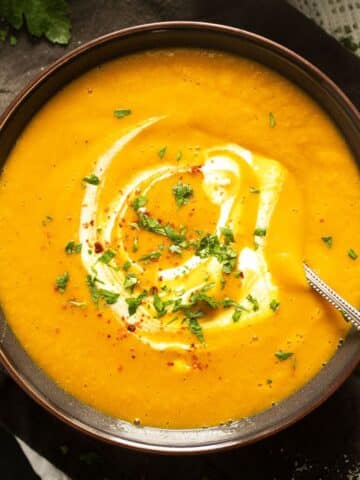 spicy carrot and lentil soup served with a little yogurt in a brown bowl.