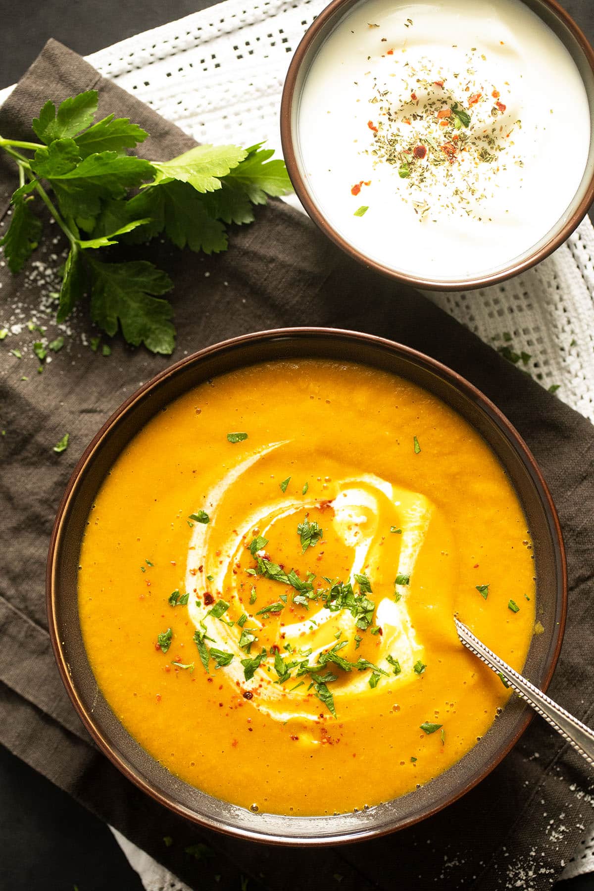 bowl of creamy lentil carrot soup and bowl of yogurt with spices on top.