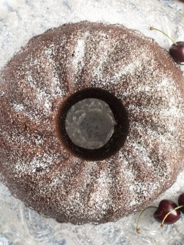 overhead view of a cherry chocolate bundt cake on a wire rack with three cherries around it.