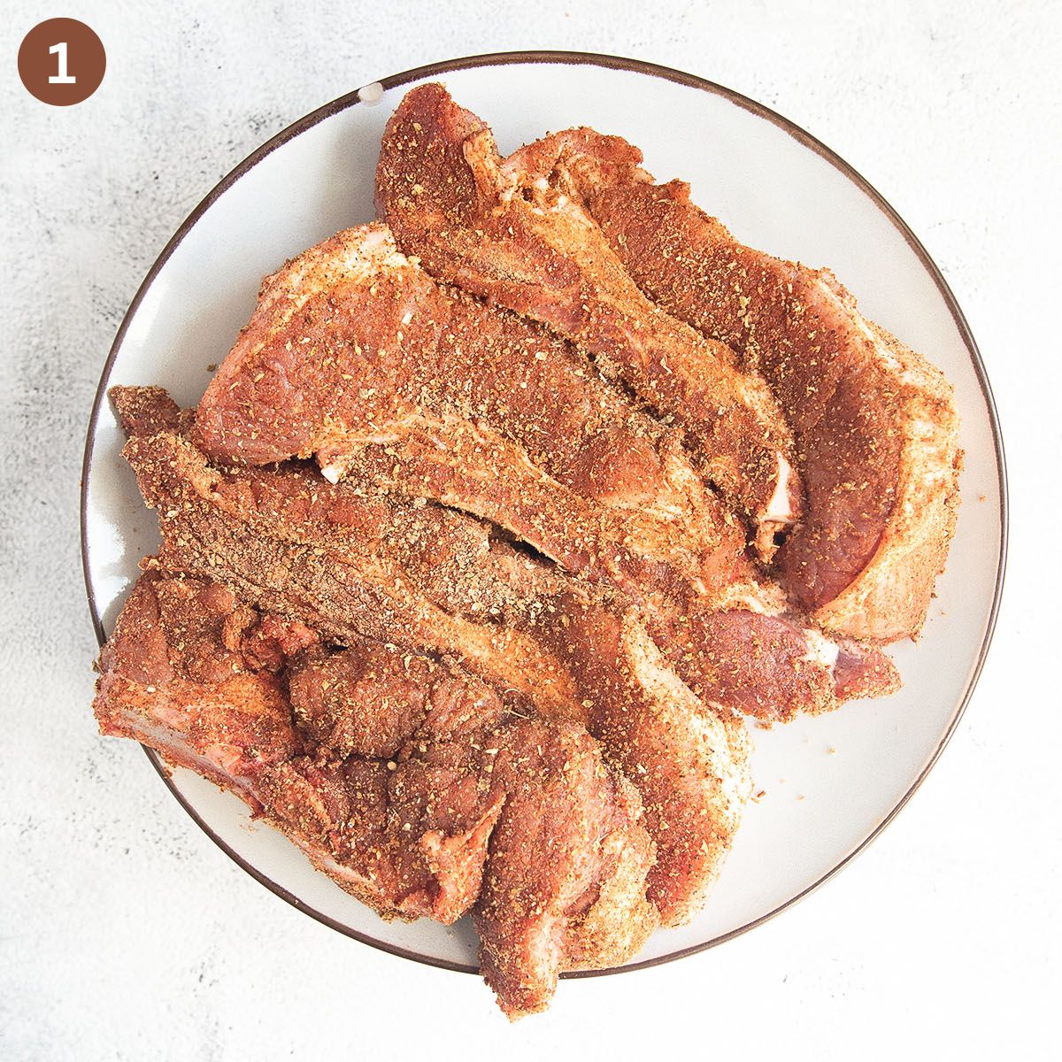 raw country style pork ribs seasoned with dry rub on a white plate.