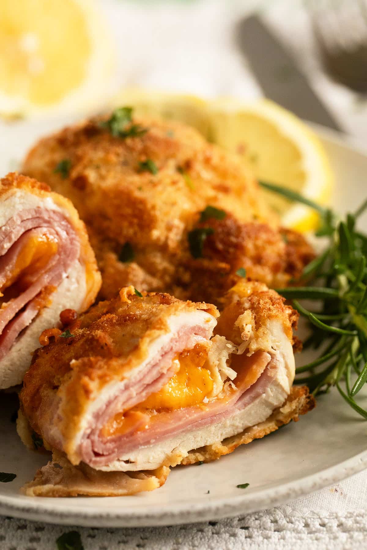 close up cheesy cordon bleu with chicken served with lemon wedges.