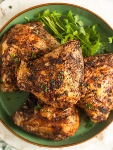 cooked air fryer frozen chicken thighs on a green plate with parsley.