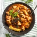 eggplant chicken stew served over polenta in a brown bowl with a spoon.