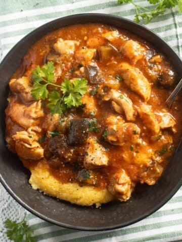 eggplant chicken stew served over polenta in a brown bowl with a spoon.