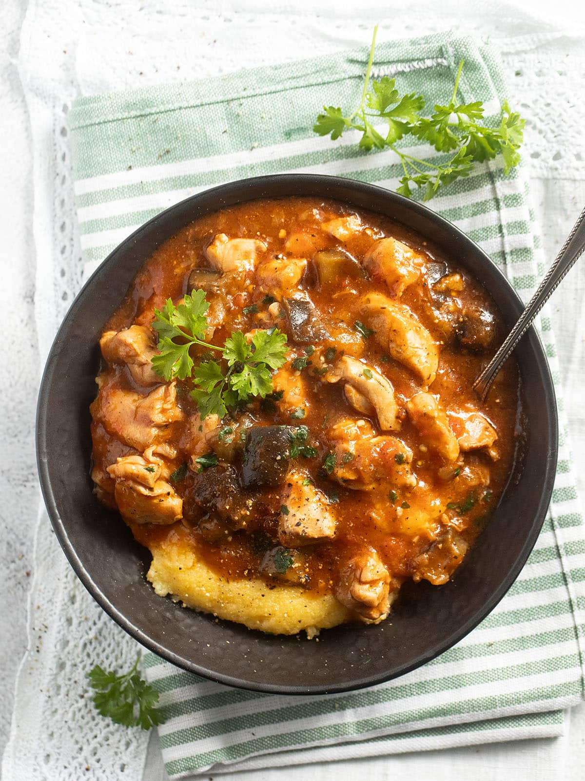 overhead view of a bowl with chicken and eggplants cooked in tomato sauce and serve with polenta.