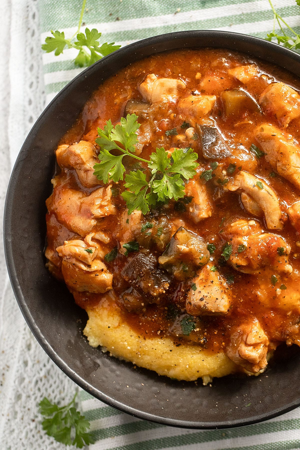 close up of chicken and eggplants in a bowl over polenta.