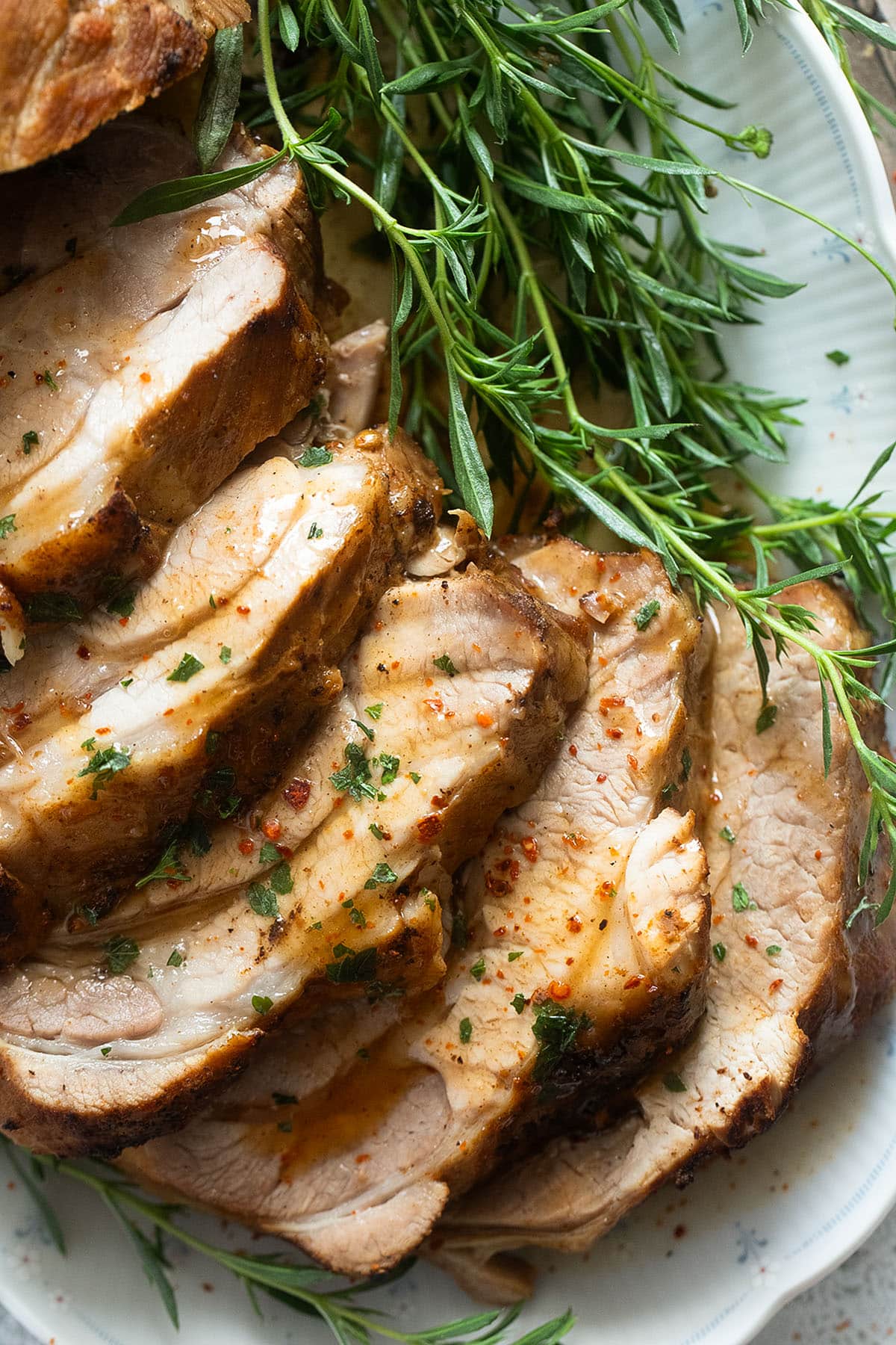 close up of sliced pork roast with a bunch of thyme sprigs.