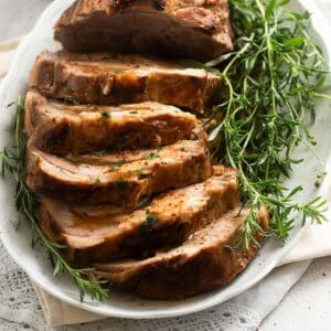 sliced pork neck on a vintage platter with a bunch of fresh thyme.