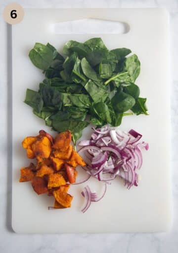 chopped spinach, roasted pumpkin and red onion on a cutting board.