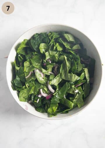 spinach leaves and red onions mixed with salad dressing in a bowl.