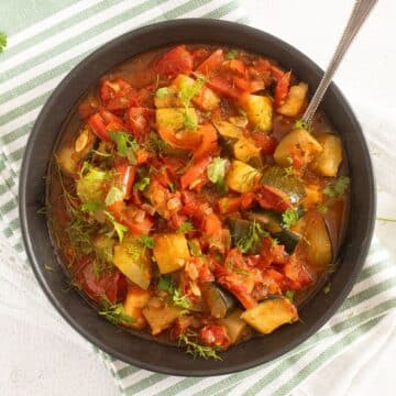 mediterranean zucchini stew in a bowl with a spoon sticking in it.