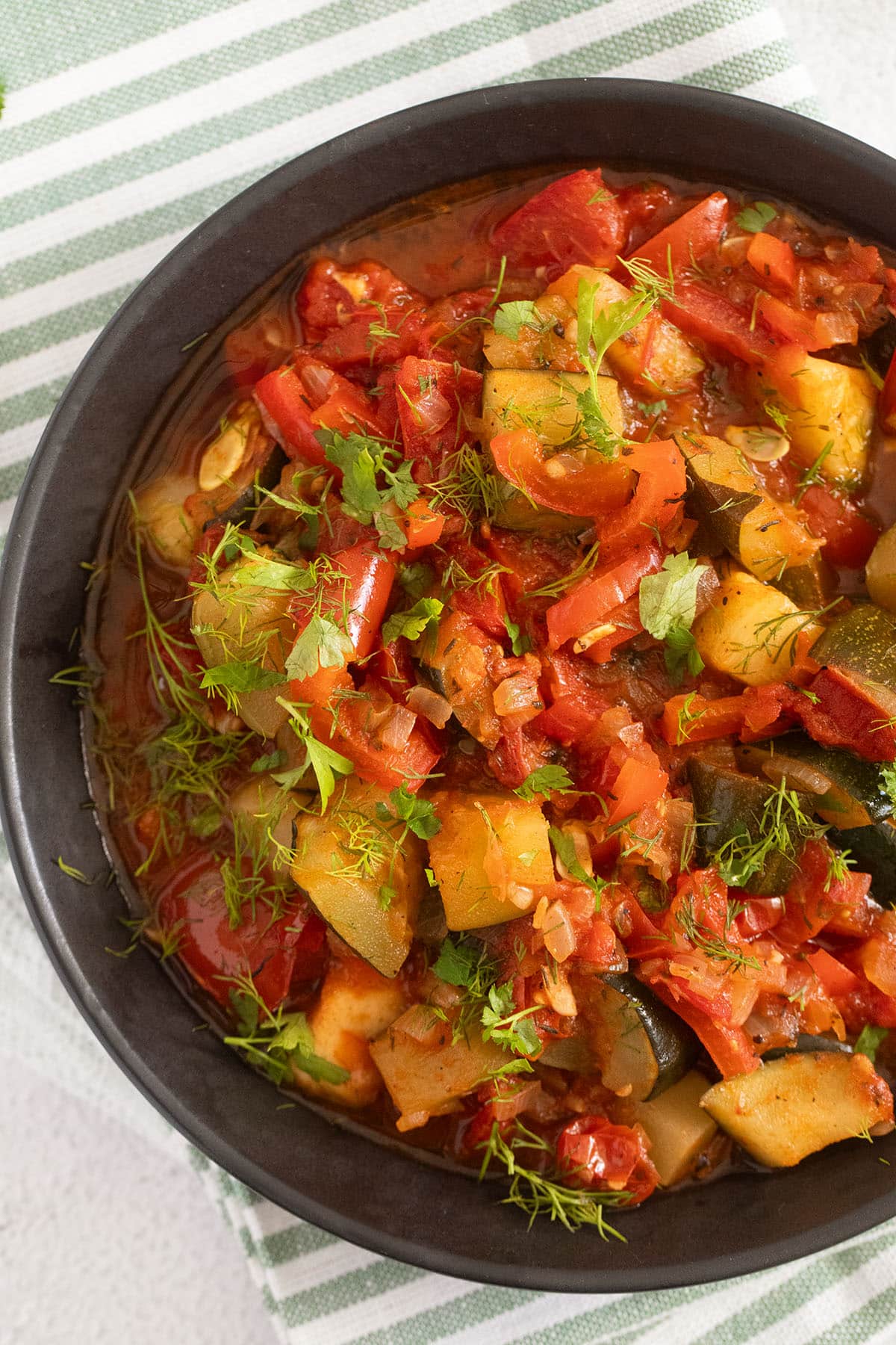 close up of a bowl with vegetable stew with zucchini, tomatoes and peppers.