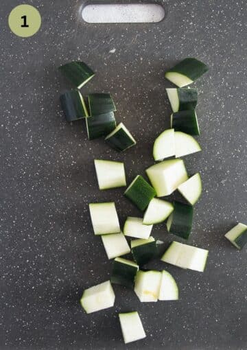 chopped zucchini cubes on a grey cutting board.