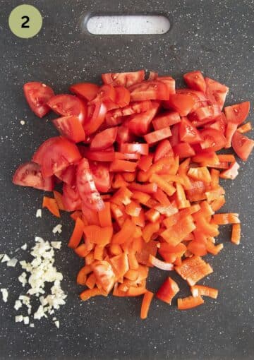 chopped tomatoes, peppers and garlic on a gray cutting board.