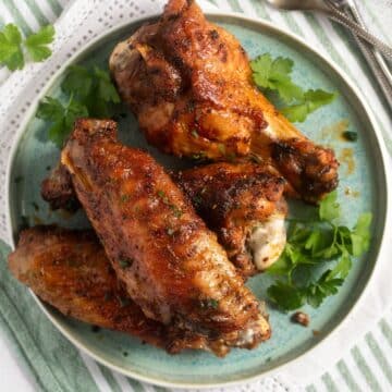 air fryer turkey wings on a blue plate with fresh parsley around it.