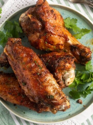 air fryer turkey wings on a blue plate with fresh parsley around it.