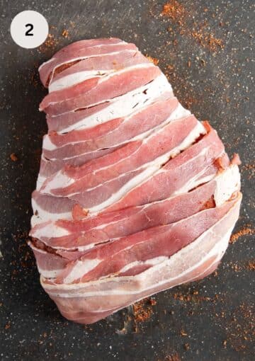 wrapping turkey breast with bacon strips on a gray cutting board.
