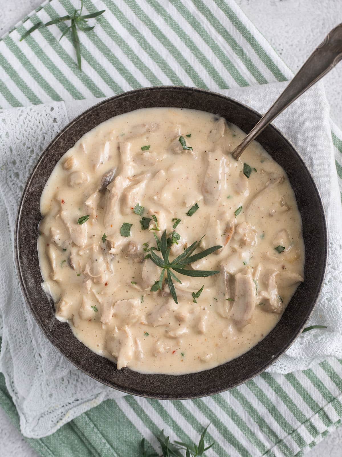 bowl with creamed turkey sprinkled with tarragon with a spoon in it.