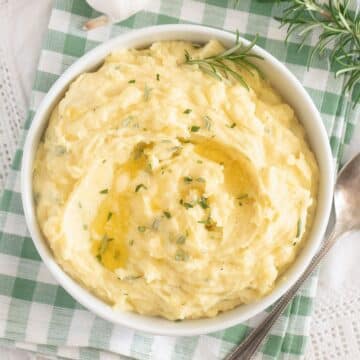 bowl with garlic and rosemary mashed potatoes on a white and green kitchen cloth.