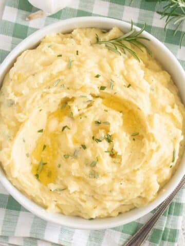 bowl with garlic and rosemary mashed potatoes on a white and green kitchen cloth.