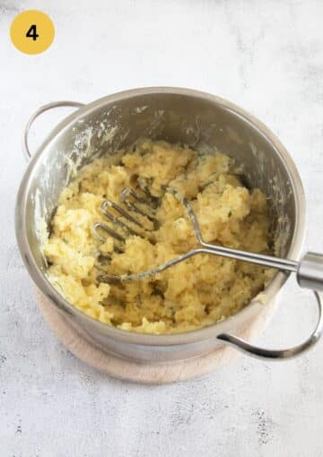 mashing potatoes with a potato masher in a pot.