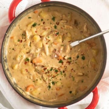 creamy turkey potato soup in a red dutch oven with a laddle in it.