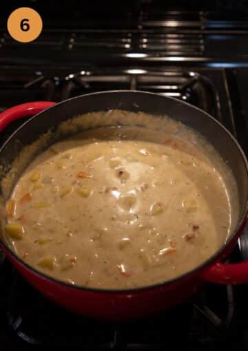 creamy soup with potatoes, cheese and turkey in a red dutch oven.