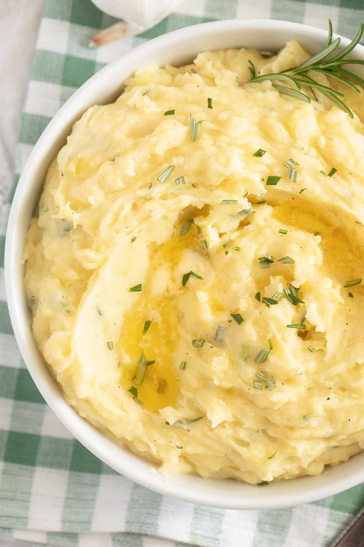 close up of mashed potatoes with melting butter and chopped rosemary on top.